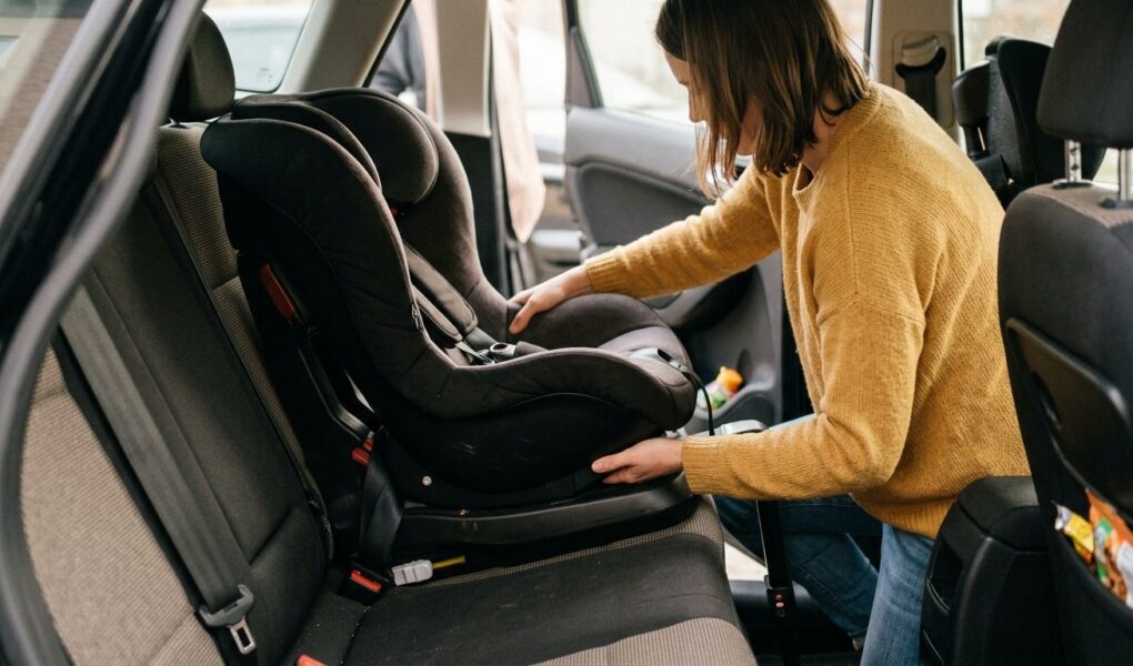 Un parent accroupi près de la banquette arrière d'une voiture, en train de vérifier manuellement le verrouillage d'une base