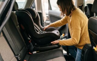 Un parent accroupi près de la banquette arrière d'une voiture, en train de vérifier manuellement le verrouillage d'une base