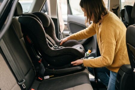 Un parent accroupi près de la banquette arrière d'une voiture, en train de vérifier manuellement le verrouillage d'une base