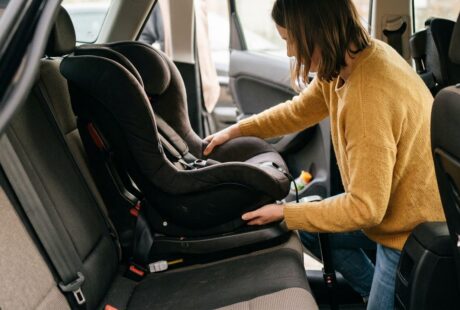 Un parent accroupi près de la banquette arrière d'une voiture, en train de vérifier manuellement le verrouillage d'une base