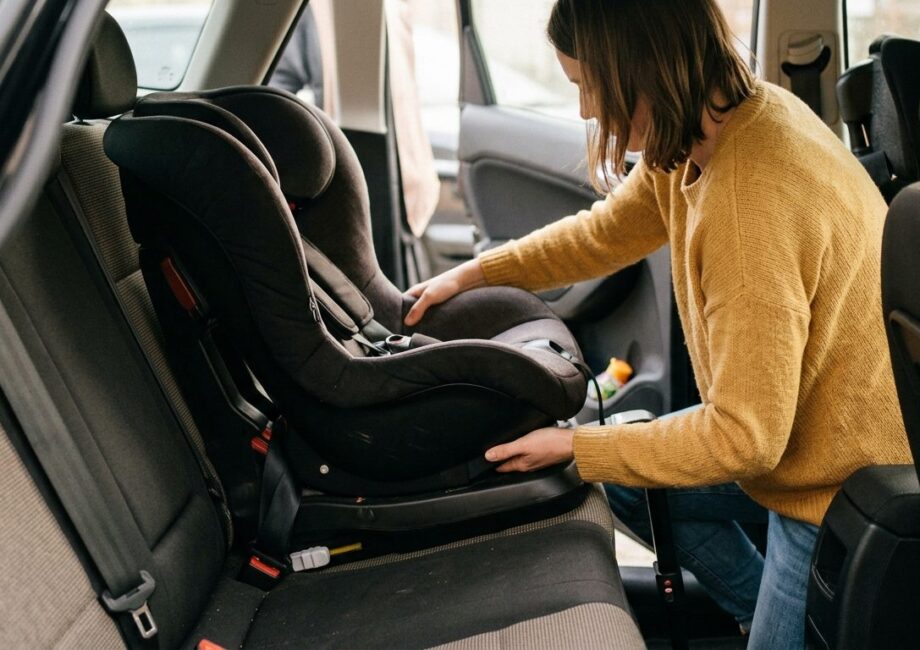 Un parent accroupi près de la banquette arrière d'une voiture, en train de vérifier manuellement le verrouillage d'une base