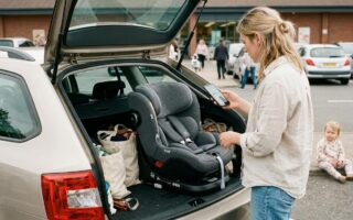 Un parent compare sur son telephone le prix d'un siege auto i-Size pose dans le coffre d'une voiture